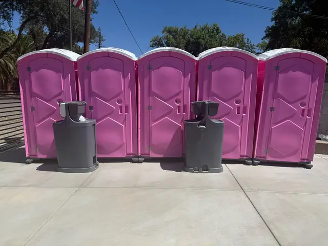 Row of pink porta potties with two handwashing stations in front