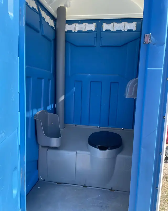 Interior of a blue standard porta potty showing the toilet seat and urinal