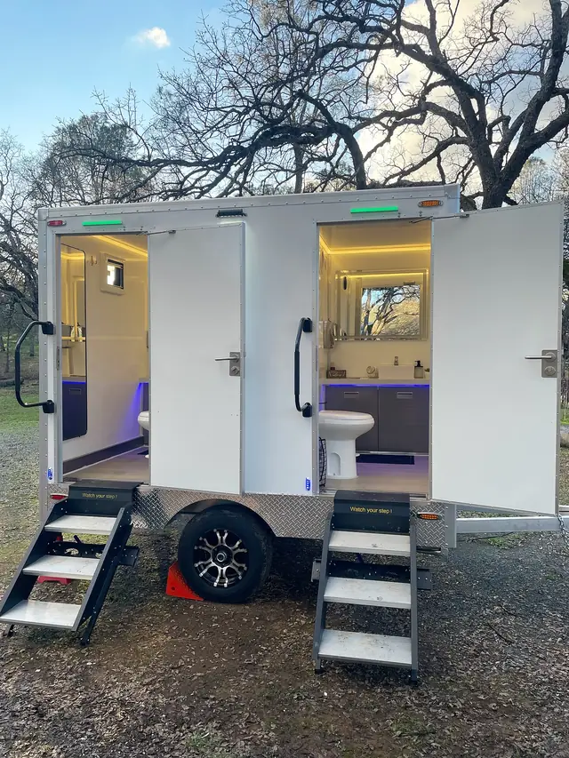 Restroom trailer with lit stalls next to a field at dusk