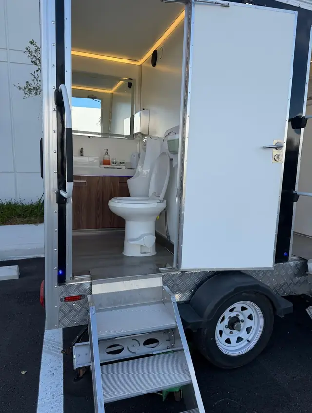 Restroom trailer with door open showing toilet and wood vanity