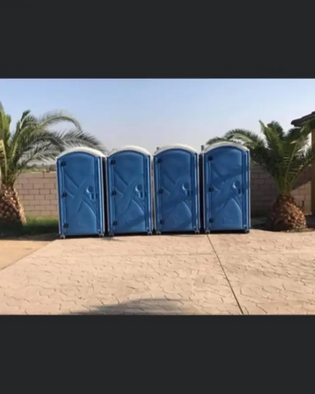 Row of four blue porta potties set on pavement between palm trees